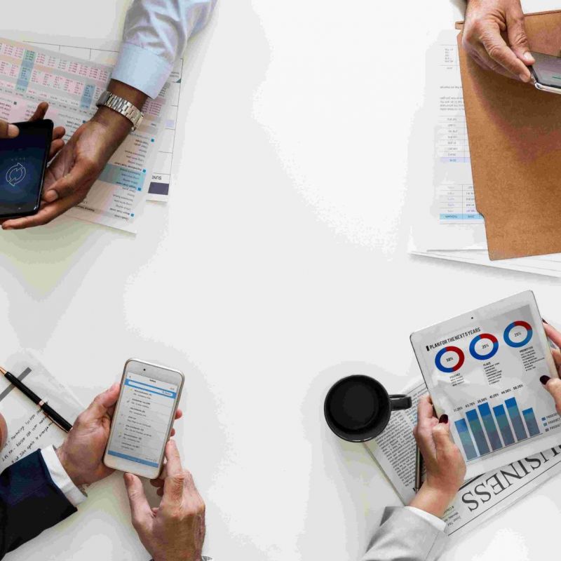 Vier Menschen sitzen am Tisch und schauen verschiedene Analysen an - auf dem Smartphone, in Mappen und auf Papier