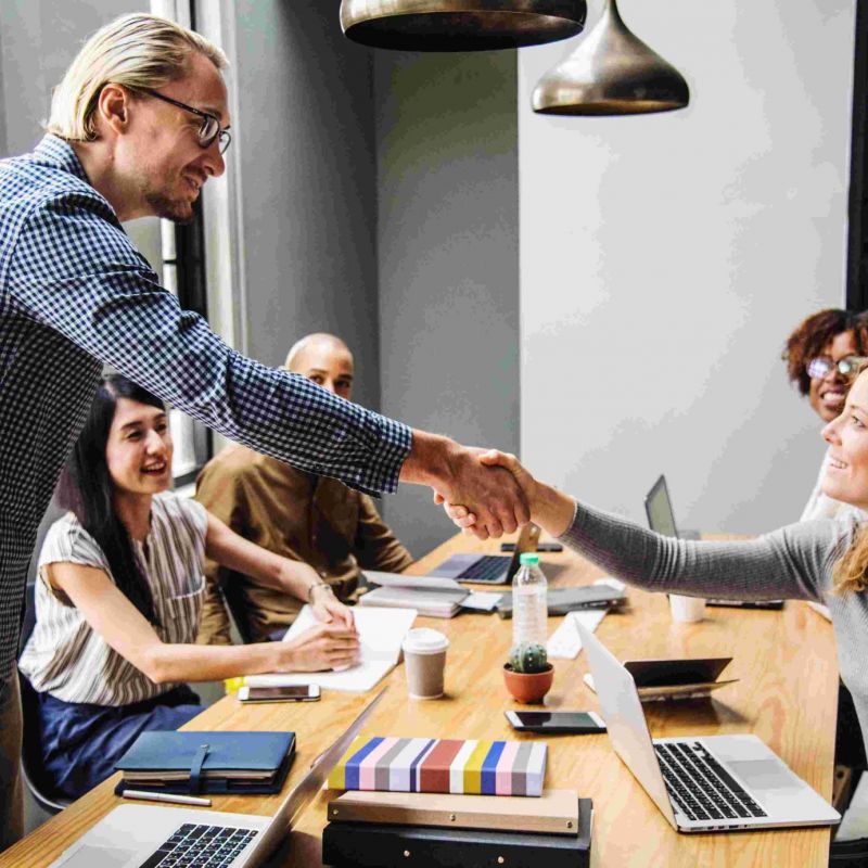 fünf Leute sitzen an einem Konferenztisch, zwei reichen sich die Hand